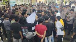 Kerumunan massa aksi berbaju hitam sedang berhadapan dan berdialog dengan barisan polisi berseragam.