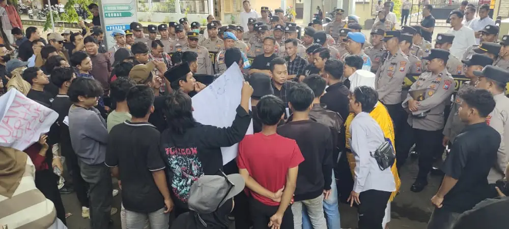 Kerumunan massa aksi berbaju hitam sedang berhadapan dan berdialog dengan barisan polisi berseragam.