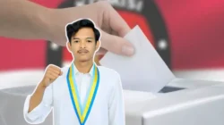 Seorang pria muda (Tijanuz Zaman) mengenakan kemeja putih dan samir organisasi PMII berwarna kuning-biru dengan pose mengepalkan tangan, berlatar belakang ilustrasi tangan memasukkan surat suara ke kotak suara dan logo KPU yang diburamkan.