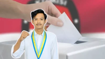 Seorang pria muda (Tijanuz Zaman) mengenakan kemeja putih dan samir organisasi PMII berwarna kuning-biru dengan pose mengepalkan tangan, berlatar belakang ilustrasi tangan memasukkan surat suara ke kotak suara dan logo KPU yang diburamkan.