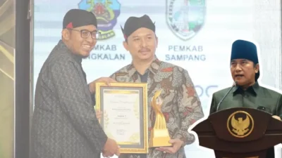 Foto kolase yang menampilkan Bupati Sumenep Achmad Fauzi Wongsojudo bersama Arif Firmanto (Kepala Bappeda sekaligus Calon Unggulan Sekda yang mundur) saat penyerahan penghargaan, bersanding dengan foto Akhmadi Yasid (Penulis Opini/Parlemen) yang sedang berpidato di podium.