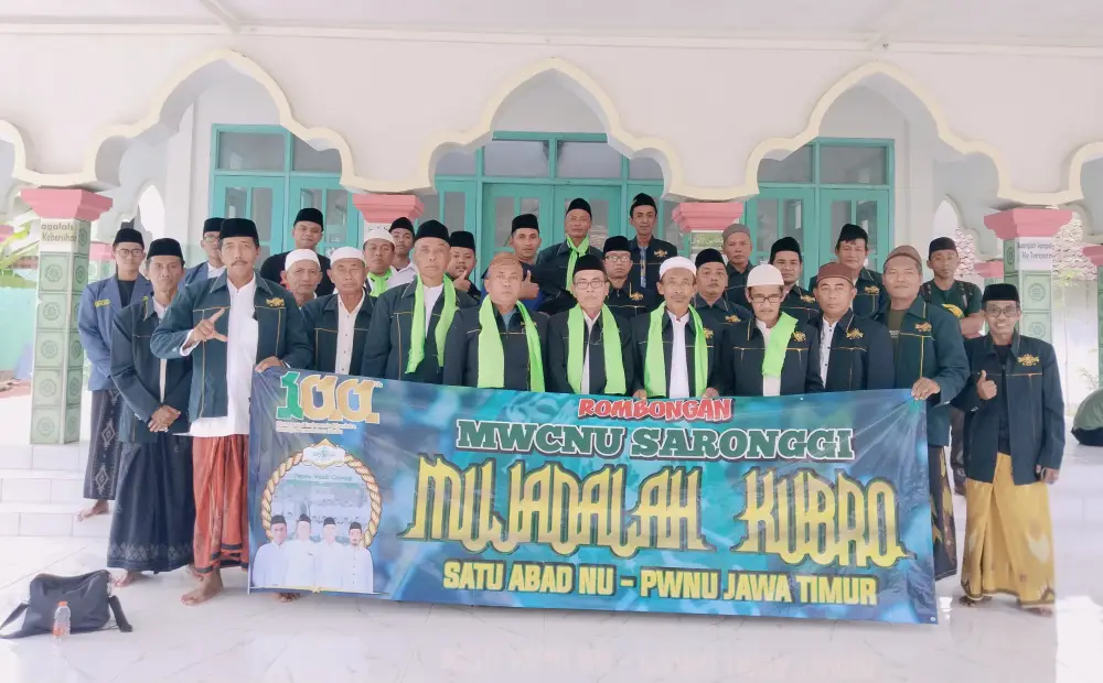 Foto bersama pengurus MWC NU Saronggi memegang spanduk bertuliskan Mujahadah Kubro Satu Abad NU PWNU Jawa Timur di depan teras masjid.