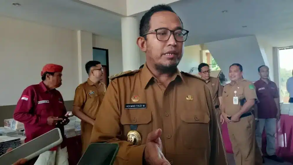 Foto Bupati, Pemkab Sumenep, Achmad Fauzi Wongsojudo, mengenakan seragam dinas cokelat sedang memberikan keterangan pers kepada wartawan di sebuah ruangan.