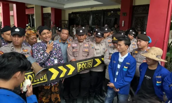 Sekretaris Daerah Kabupaten Sumenep, Agus Dwi Saputra, sedang berbicara menggunakan mikrofon di hadapan massa aksi PMII dan barisan kepolisian di depan Kantor Pemkab Sumenep.