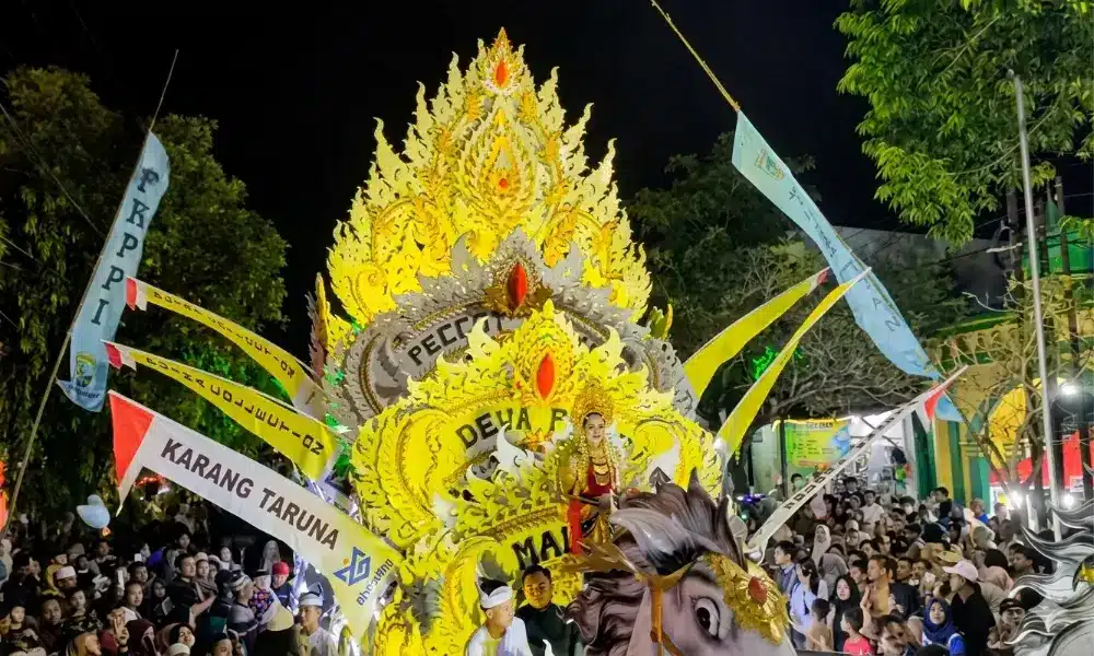 Kemeriahan Parade Musik Tong Tong di Sumenep yang menampilkan dekorasi kereta kencana raksasa bernuansa emas dan kuning menyala, lengkap dengan patung kepala kuda di bagian depan, serta dipadati oleh ribuan warga di kanan kiri jalan pada malam hari.