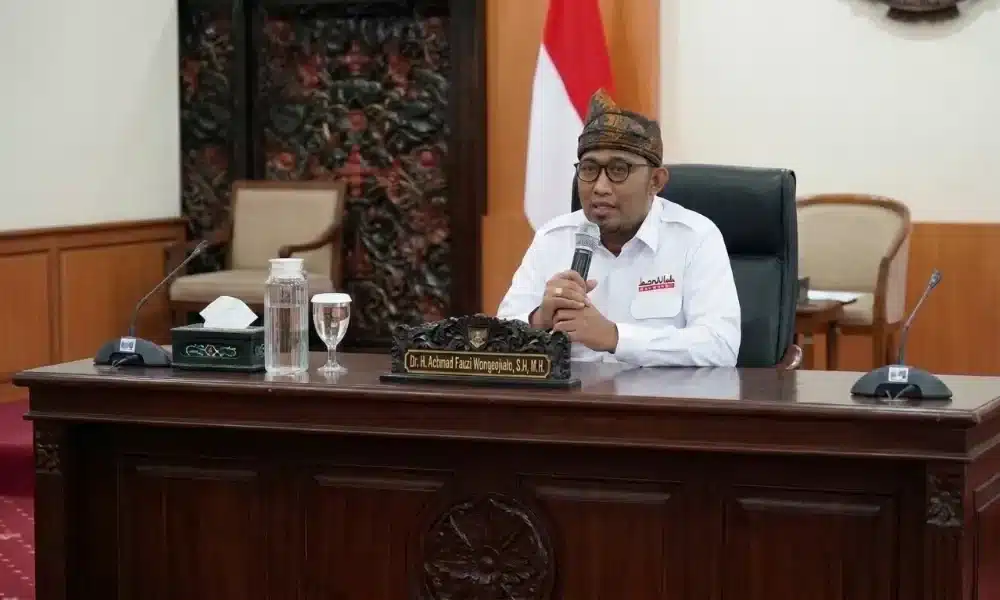 Bupati Sumenep, Achmad Fauzi Wongsojudo, mengenakan kemeja putih dan blangkon khas, sedang berbicara menggunakan mikrofon saat memimpin rapat kedinasan di ruang kerja Pemerintah Kabupaten Sumenep.