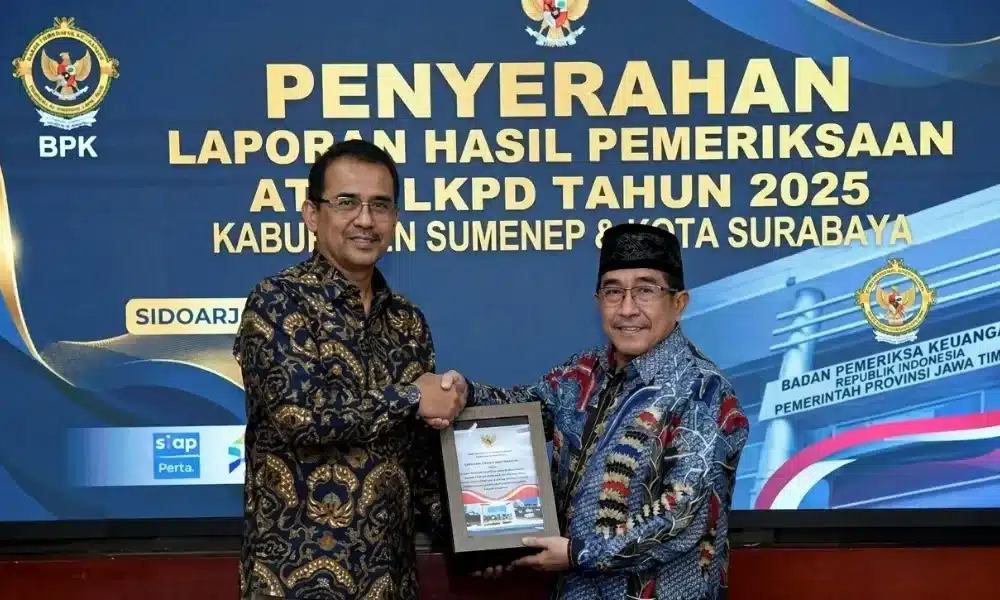 Foto Wabup Sumenep KH. Imam Hasyim (kanan) mewakili Pemkab Sumenep bersama perwakilan BPK RI (kiri) sedang berjabat tangan sambil memegang bingkai Laporan Hasil Pemeriksaan (LHP). Di latar belakang terdapat spanduk biru besar bertuliskan "PENYERAHAN LAPORAN HASIL PEMERIKSAAN ATAS LKPD TAHUN 2025 KABUPATEN SUMENEP & KOTA SURABAYA" dengan logo BPK.