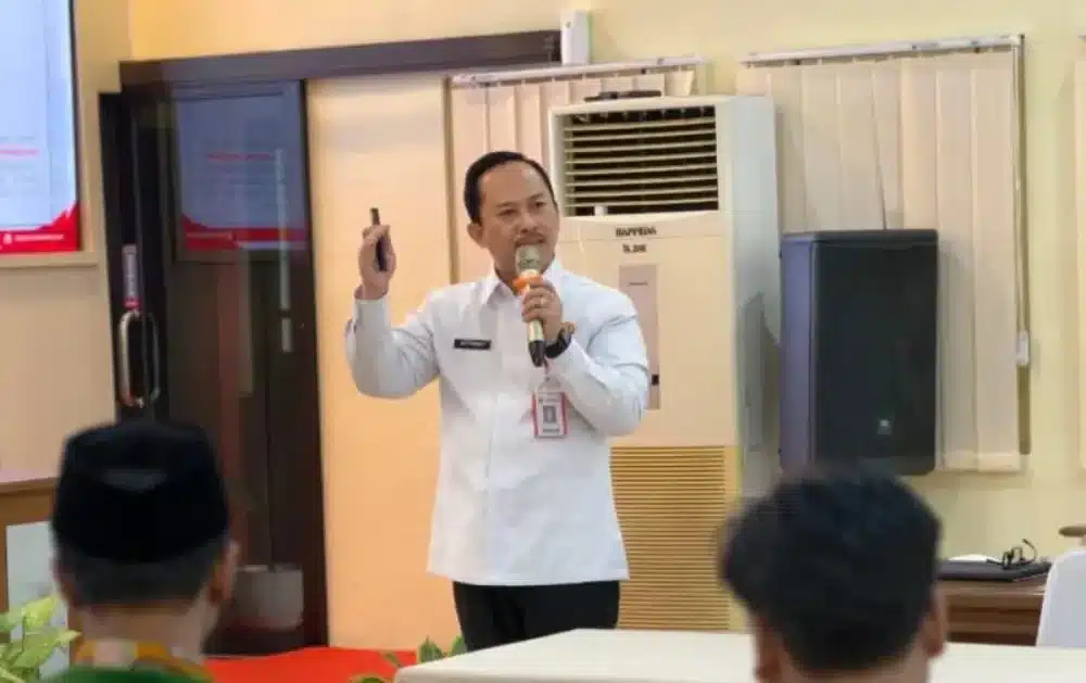 Kepala Bappeda Sumenep, Arif Firmanto, sedang berbicara menggunakan mikrofon saat memaparkan kebijakan Pemkab Sumenep terkait penguatan ekonomi kerakyatan dalam sebuah forum sosialisasi.