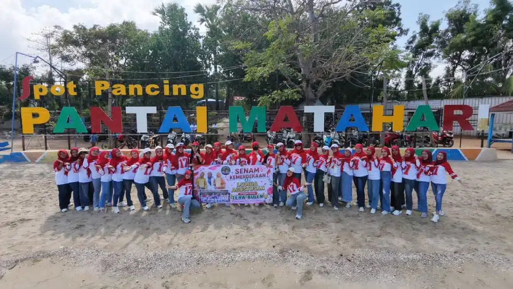 Puluhan perempuan anggota Sanggar Senam Tera’ Bulen berfoto bersama mengenakan seragam baju merah putih di depan papan tulisan "PANTAI MATAHARI" sambil membentangkan spanduk kegiatan "Senam Kemerdekaan & Lomba Agustusan".